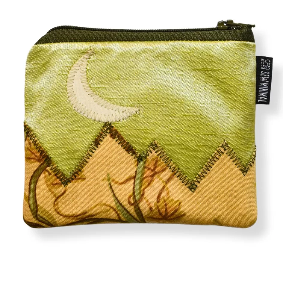 A small, green coin pouch with a crescent moon and mountain applique.