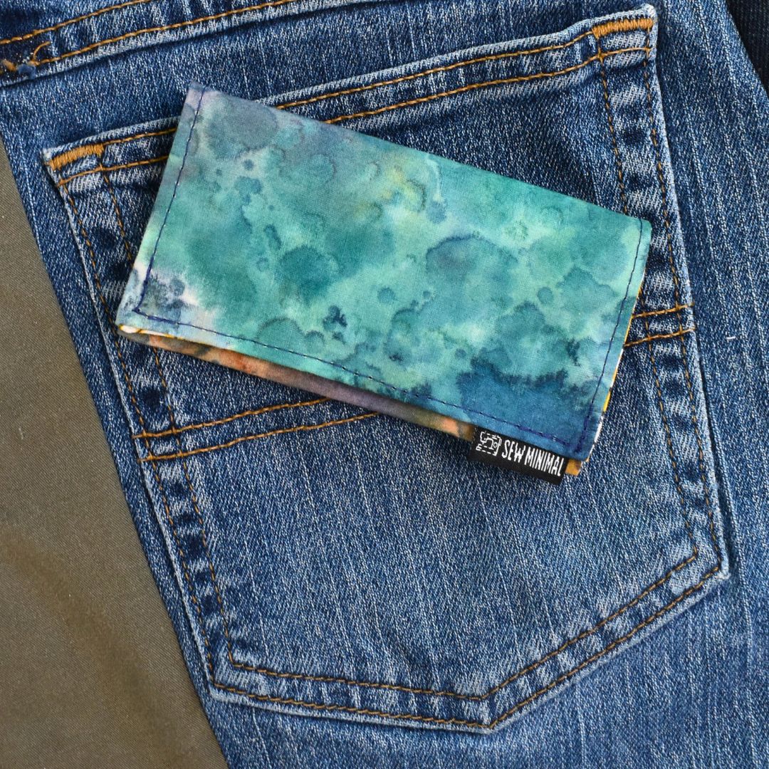 Cloudy sky print small cardholder wallet laying on a blue jean back pocket.