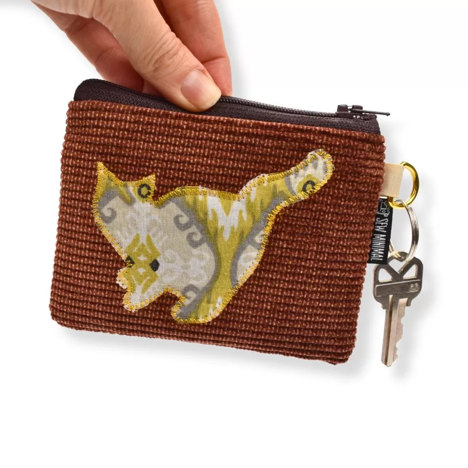 The image shows a small brown woven zipper pouch with a decorative yellow and white fabric patch in the shape of a cat on the front. The pouch is being held by a hand and has a key attached to a metal ring on the side. The zipper appears DARK BROWN, and there is a small fabric tag near the key with the text "SEW MINIMAL."